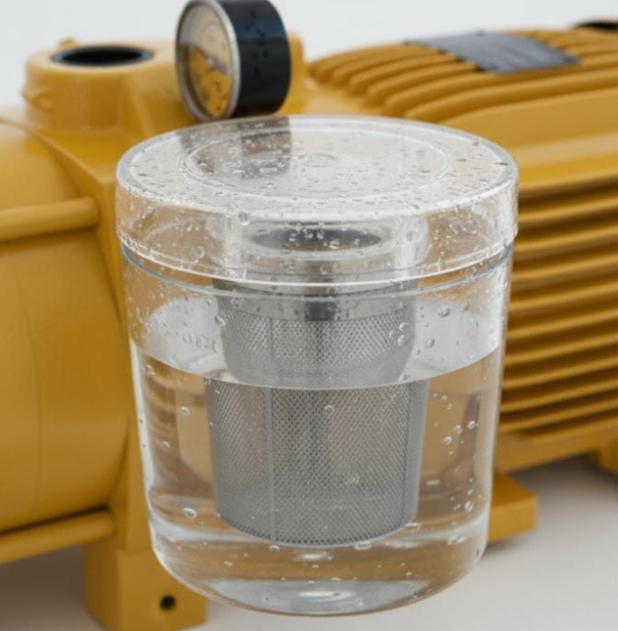 Close-up de pré-filtro transparente de bomba de piscina com água límpida e cesto interno metálico em destaque.